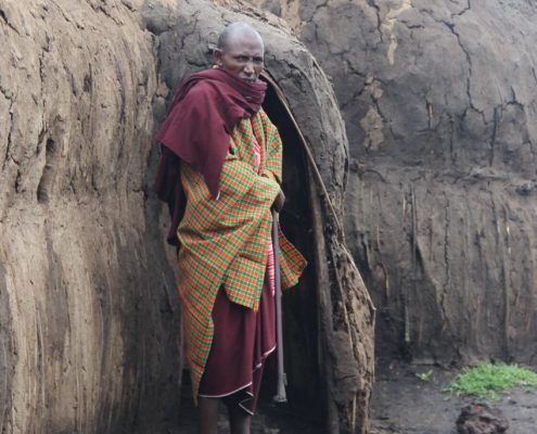 Lors de votre safari de 7 jours en Tanzanie, vous aurez l'occasion de rencontrer et d'apprendre à connaître la population et la culture locales, comme ce Maasai âgé qui se tient devant un Boma traditionnel fait d'adobe.